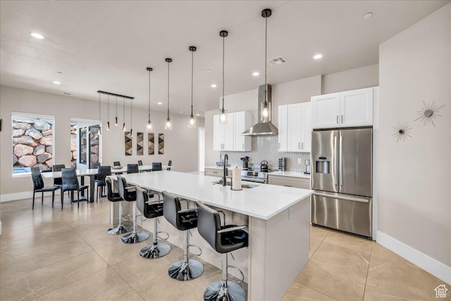 kitchen featuring tasteful backsplash, visible vents, stainless steel fridge with ice dispenser, wall chimney exhaust hood, and a sink