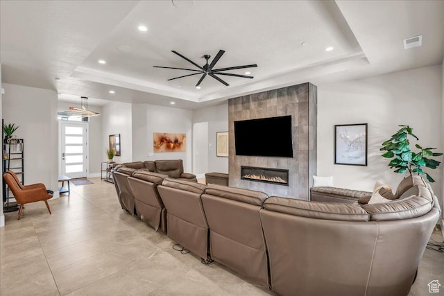 living room featuring a tile fireplace, a raised ceiling, visible vents, and recessed lighting
