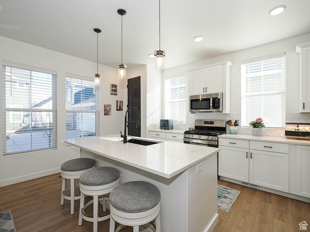 kitchen featuring a center island with sink, tasteful backsplash, appliances with stainless steel finishes, a sink, and wood finished floors