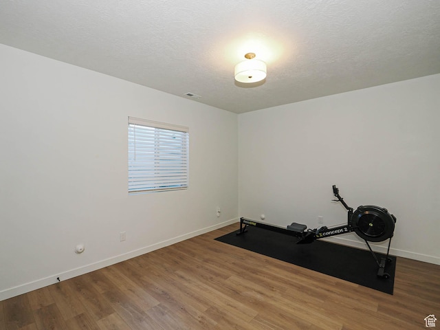 workout room with a textured ceiling, wood finished floors, visible vents, and baseboards