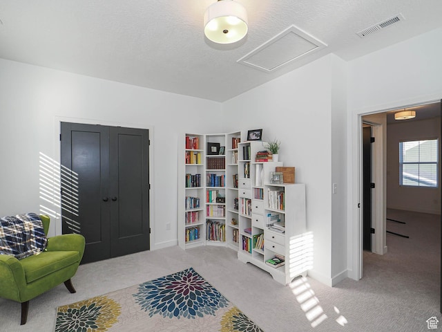 sitting room featuring a textured ceiling, carpet flooring, visible vents, baseboards, and attic access