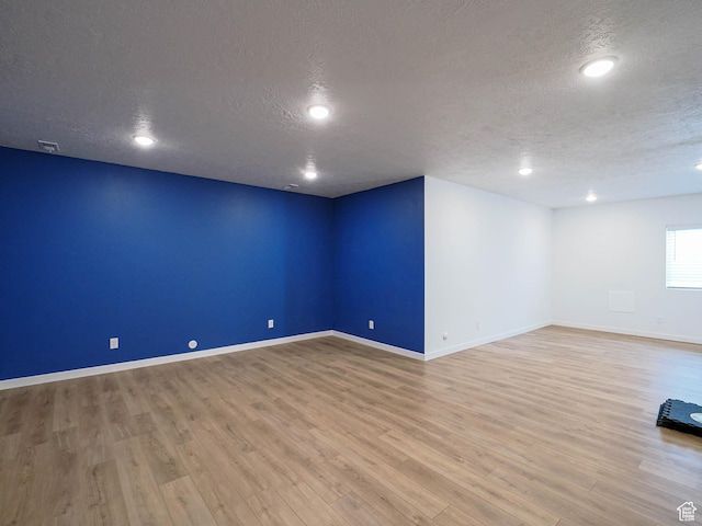 below grade area with a textured ceiling, wood finished floors, visible vents, and baseboards
