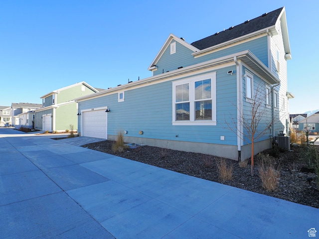view of side of home with a garage, a residential view, driveway, and central air condition unit