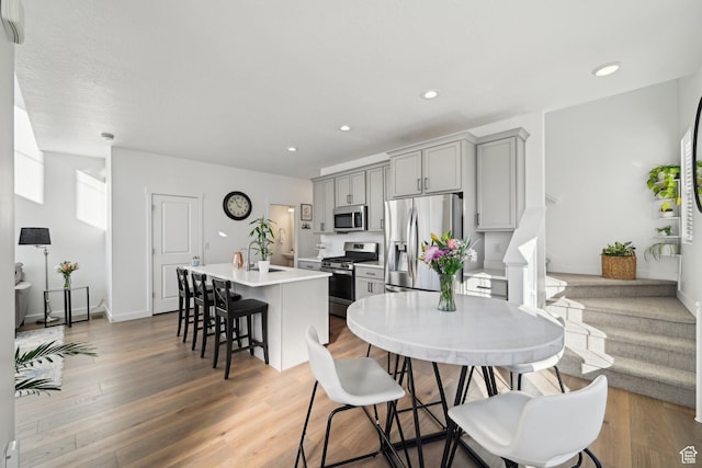 kitchen with a center island with sink, wood finished floors, stainless steel appliances, light countertops, and gray cabinetry