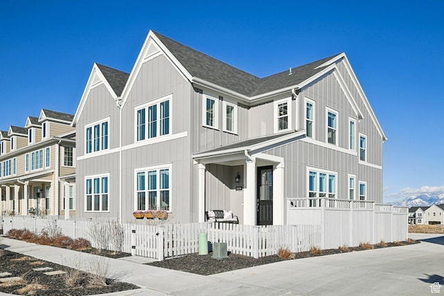 view of front of house with roof with shingles, a fenced front yard, board and batten siding, and a residential view