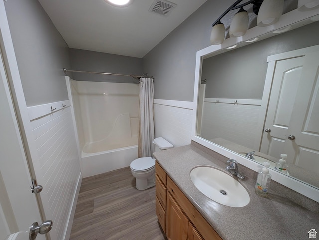 bathroom with wood finished floors, a wainscoted wall, toilet, vanity, and shower / bath combination with curtain