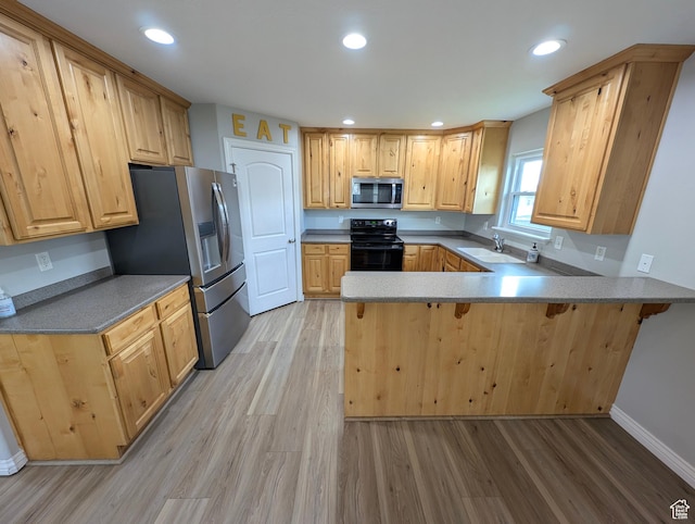 kitchen with appliances with stainless steel finishes, light wood-style flooring, a peninsula, a kitchen bar, and recessed lighting