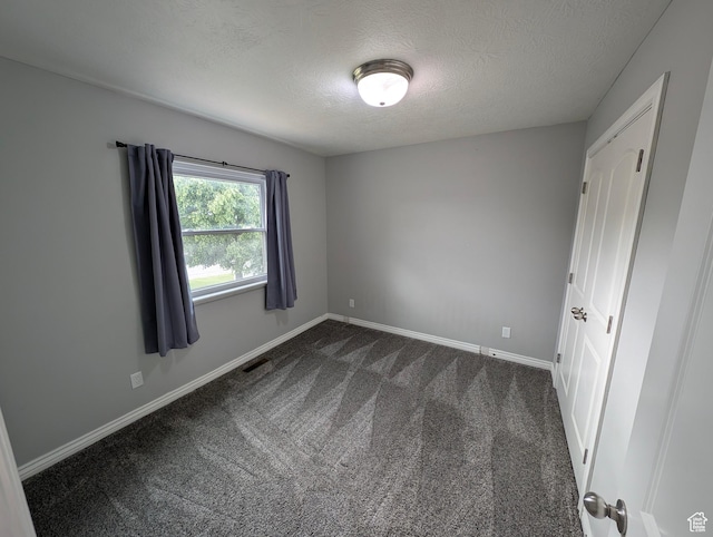 empty room with a textured ceiling, baseboards, and dark carpet