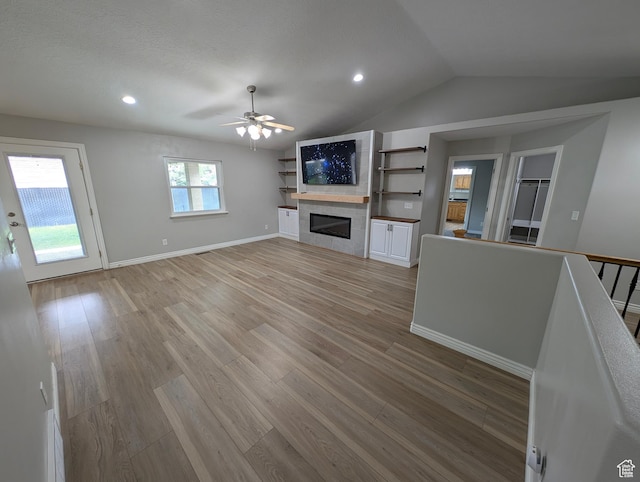 unfurnished living room featuring a ceiling fan, lofted ceiling, light wood-style flooring, a tile fireplace, and recessed lighting