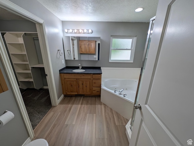 full bathroom featuring wood finished floors, a textured ceiling, vanity, and a garden tub
