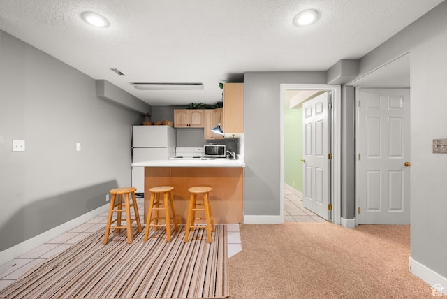 kitchen with stainless steel microwave, freestanding refrigerator, a peninsula, a textured ceiling, and a kitchen bar