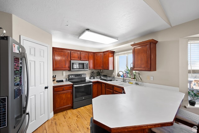 kitchen featuring light wood finished floors, a peninsula, stainless steel appliances, light countertops, and a sink