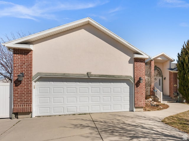 view of front facade with a garage, driveway, brick siding, and stucco siding