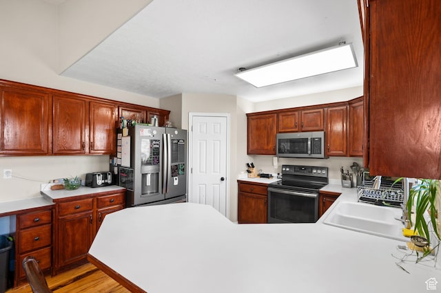 kitchen with a peninsula, a sink, light countertops, appliances with stainless steel finishes, and light wood finished floors