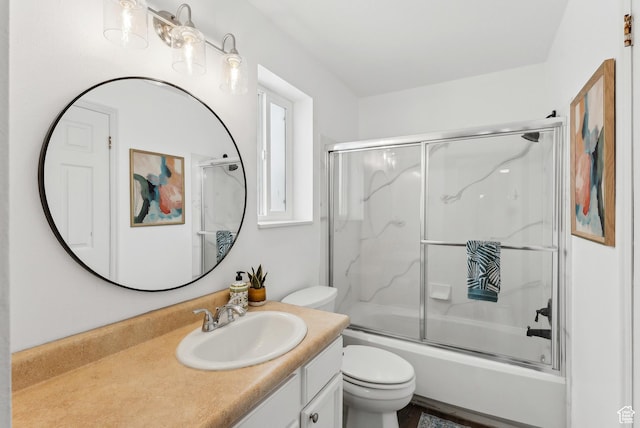 bathroom featuring toilet, combined bath / shower with glass door, and vanity