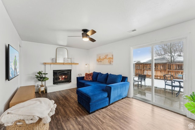 living room featuring ceiling fan, visible vents, a fireplace, and wood finished floors