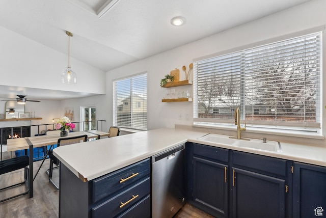 kitchen with a warm lit fireplace, a peninsula, a sink, stainless steel dishwasher, and blue cabinetry