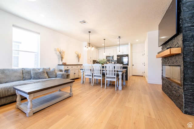 695 W Claystone Dr, St George, UT 84790 - living room featuring a textured ceiling, a stone fireplace, visible vents, light wood-type flooring, and an inviting chandelier