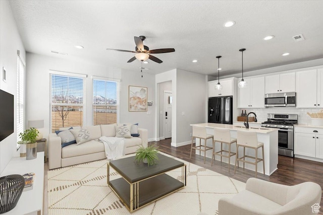 living room featuring a textured ceiling, recessed lighting, dark wood-type flooring, visible vents, and a ceiling fan