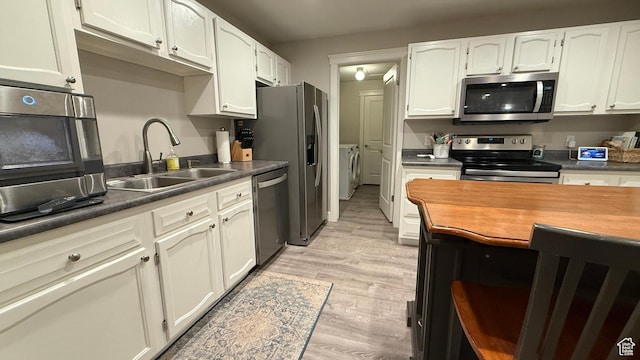 kitchen featuring stainless steel appliances, light wood-style floors, white cabinetry, a sink, and separate washer and dryer