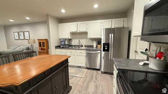 kitchen featuring stainless steel appliances, dark countertops, a sink, and white cabinetry