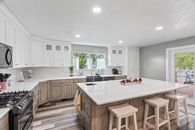 2490 W 12195 S, Riverton, UT 84065 - kitchen featuring black appliances, light wood-style flooring, a center island with sink, a kitchen breakfast bar, and light countertops