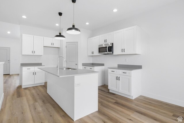271 N 1160 N Unit 32, Tooele, UT 84074 - kitchen featuring a center island with sink, stainless steel microwave, light wood-style floors, white cabinetry, and a sink