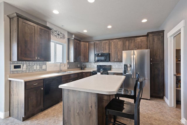 kitchen with a breakfast bar area, dark brown cabinetry, a sink, light countertops, and black appliances