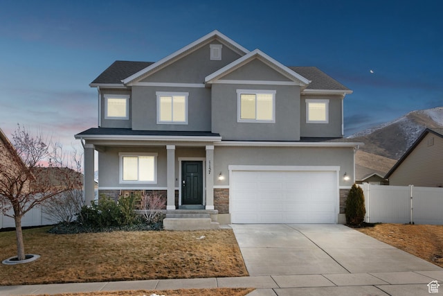 craftsman house featuring an attached garage, stone siding, fence, and stucco siding