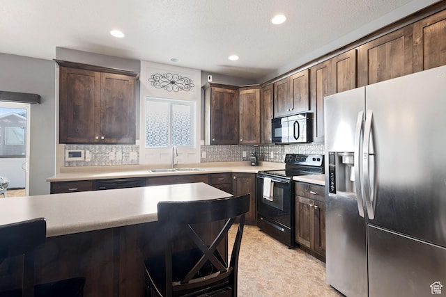 kitchen featuring a breakfast bar area, a sink, light countertops, decorative backsplash, and black appliances