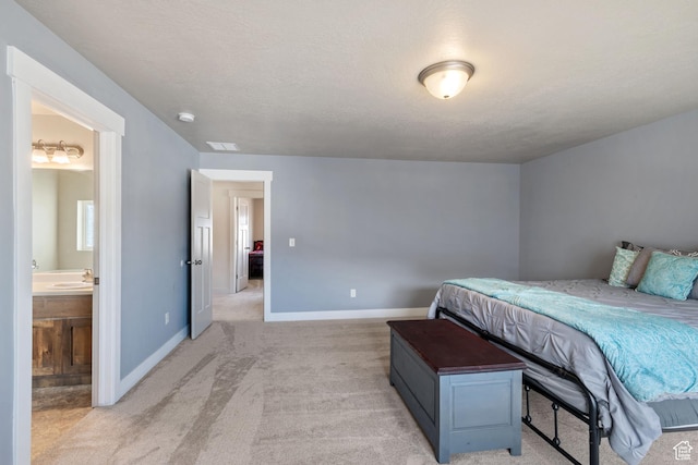bedroom featuring light colored carpet, a textured ceiling, baseboards, and ensuite bathroom