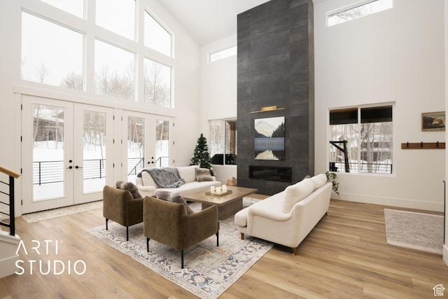 living area with plenty of natural light, light wood-style flooring, a large fireplace, and french doors