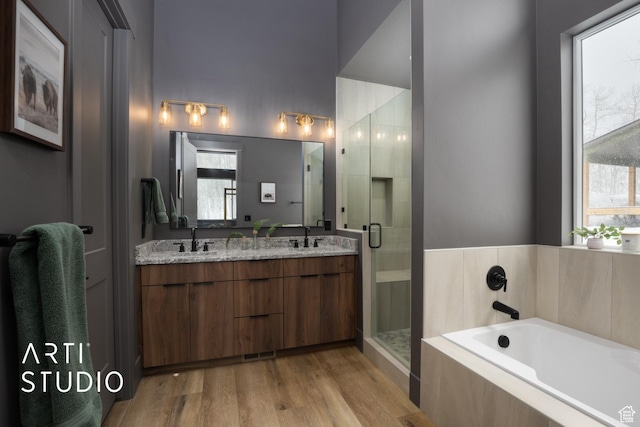 bathroom featuring a stall shower, a garden tub, a sink, and wood finished floors