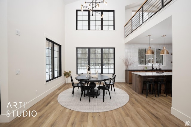 dining space featuring a towering ceiling, an inviting chandelier, light wood-style flooring, and baseboards