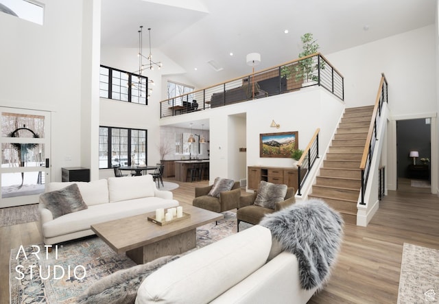 living room featuring high vaulted ceiling, light wood-style flooring, an inviting chandelier, and stairs