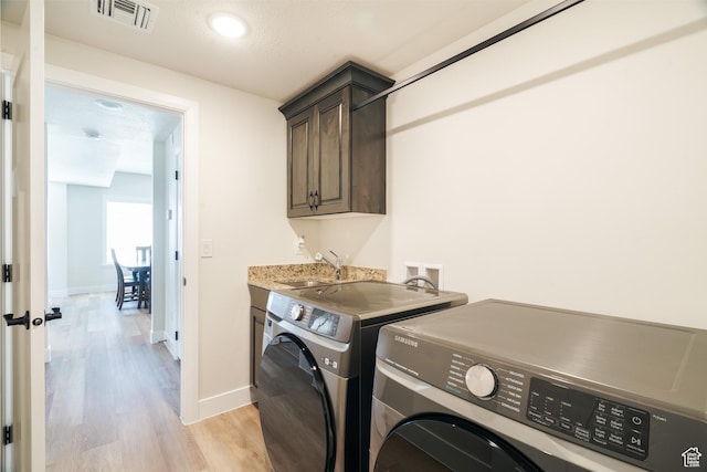 1044 E Southern Homestead Blvd, Enoch, UT 84721 - laundry room featuring light wood finished floors, visible vents, cabinet space, washing machine and dryer, and a sink