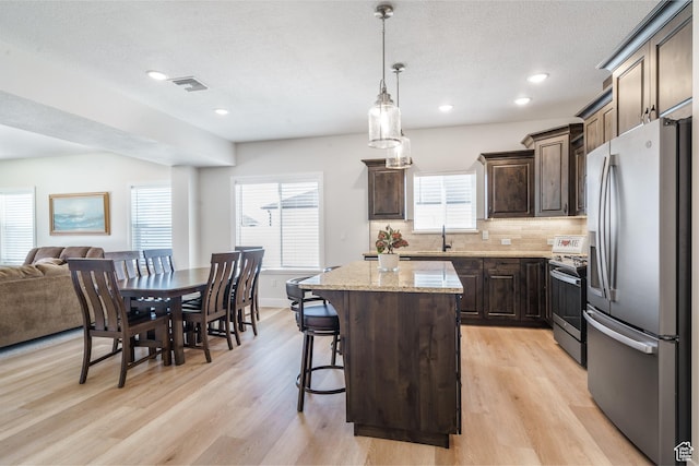 1044 E Southern Homestead Blvd, Enoch, UT 84721 - kitchen with dark brown cabinetry, tasteful backsplash, light wood finished floors, appliances with stainless steel finishes, and a center island