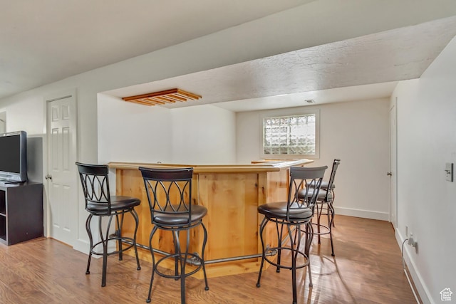 bar with a dry bar, wood finished floors, and baseboards
