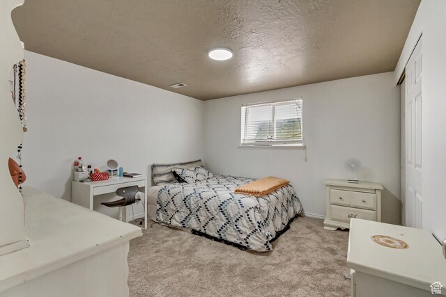 bedroom with a textured ceiling, a closet, visible vents, and light colored carpet