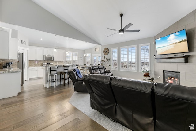 living room featuring lofted ceiling, a tiled fireplace, wood finished floors, and a ceiling fan