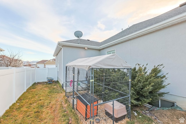 exterior space with roof with shingles, a fenced backyard, a lawn, and stucco siding