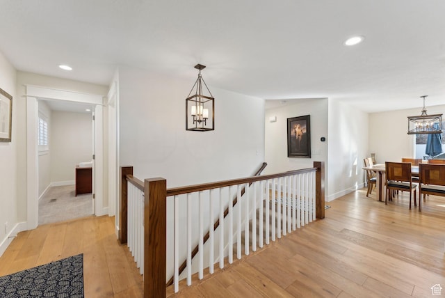hall featuring light wood-style flooring, an upstairs landing, and an inviting chandelier