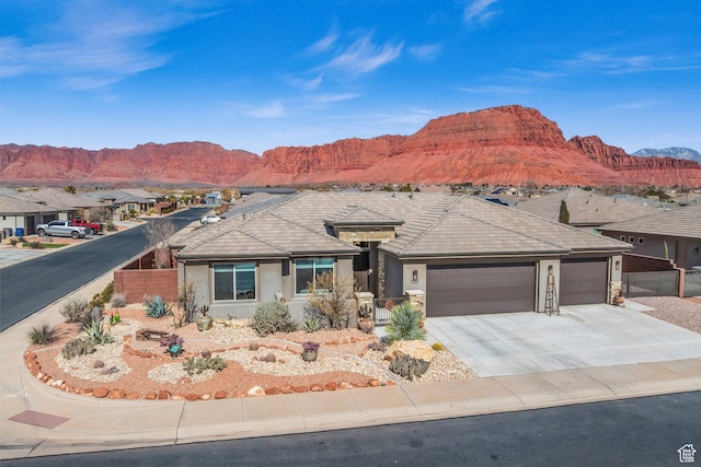 ranch-style house featuring concrete driveway, stucco siding, fence, an attached garage, and a mountain view
