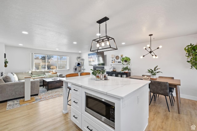 kitchen with light wood-style floors, white cabinetry, stainless steel microwave, and a center island