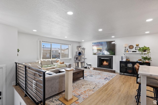 living area with baseboards, wood finished floors, a lit fireplace, a textured ceiling, and recessed lighting