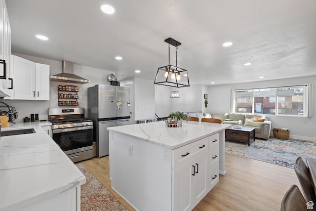 kitchen with light wood-style flooring, stainless steel appliances, a kitchen island, open floor plan, and wall chimney range hood