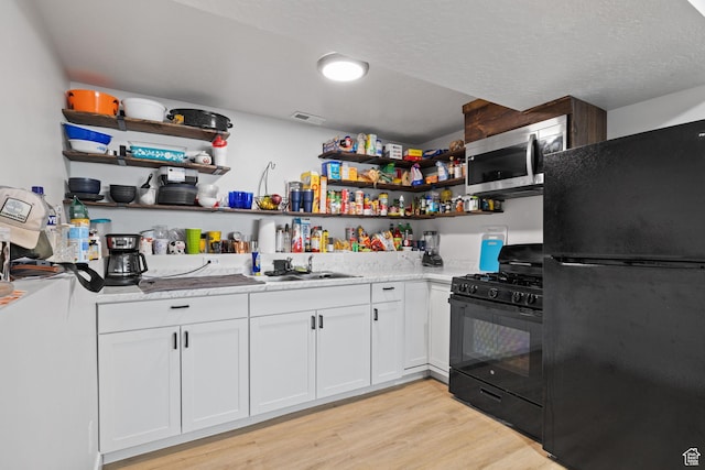 kitchen featuring light wood finished floors, open shelves, white cabinets, a sink, and black appliances