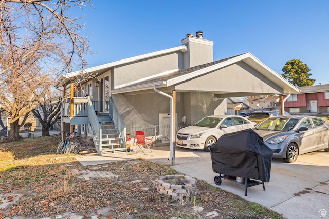 back of house with an outdoor fire pit, a chimney, stairway, a carport, and stucco siding