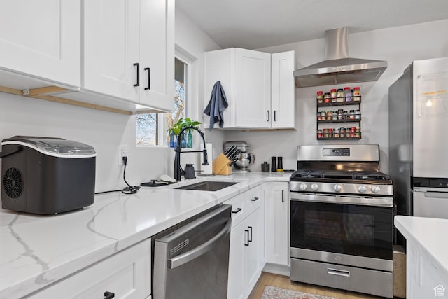kitchen featuring stainless steel appliances, white cabinetry, a sink, and wall chimney exhaust hood