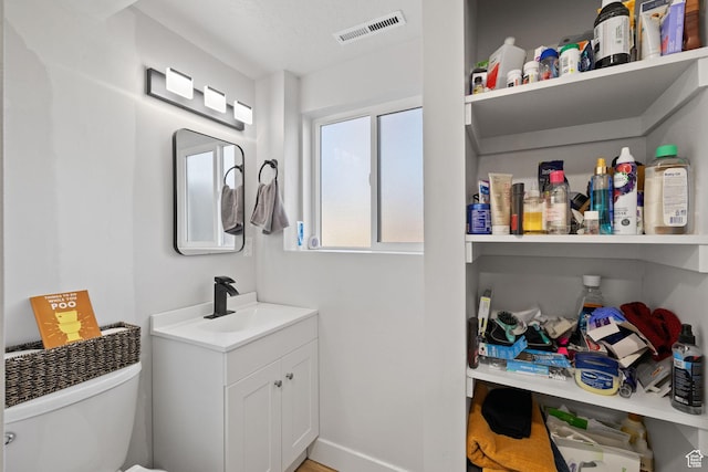 half bathroom with toilet, baseboards, visible vents, and vanity